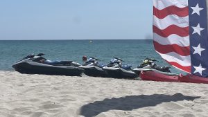 View larger photo: Several jetskis on a beach with a red and white stripped and white star on blue background flag on the left foreground (Miami Beach, Florida)