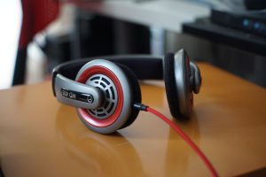 View larger photo: Close-up image of a pair of over-ear headphones with red accents and a red cable placed on a metal surface. The background is blurred, showing parts of an office interior.