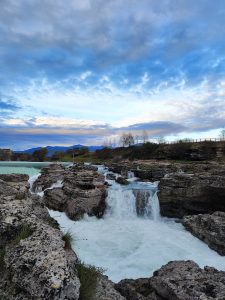 View of the Niagara Falls in Podgorica, Montenegro with mountains in the background and a cloudy sky.