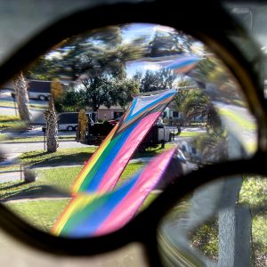 a progress pride flag on a flag pole flying in the center of the image. The image is taken through a stained glass window, so the flag is slightly warped.