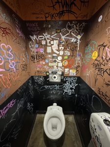 The inside of a bathroom stall with walls covered in graffiti and stickers.