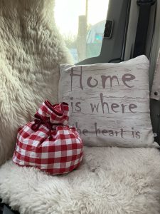 Red gingham pouch on a fluffy blanket. With a cushion that says "home is where the heart is"