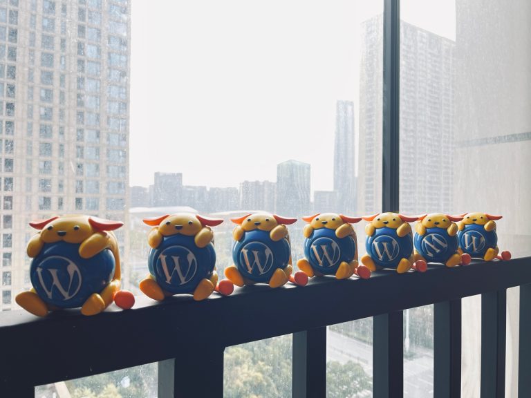 Wapuu toys on the railing in front of a window. Highrises can be seen in the background.