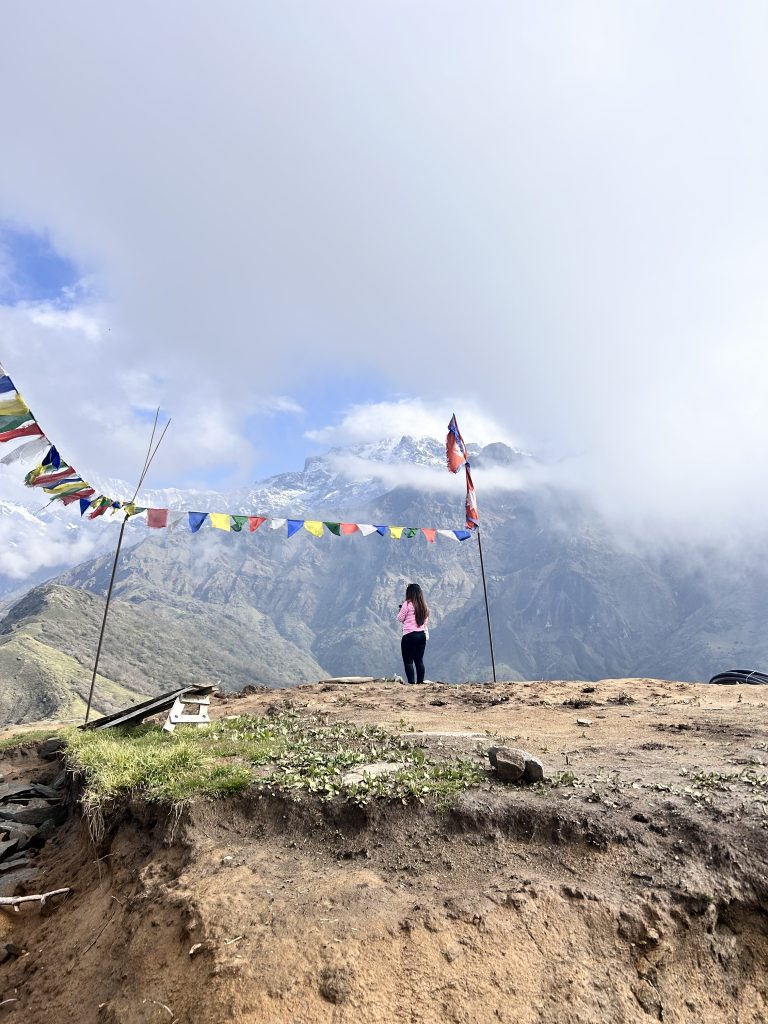 A female trekker standing near to the Nepal flag and cloudy mountain Infront.