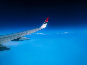 Wing of aeroplane on a bright blue sky. A few small fluffy clouds on the horizon. 