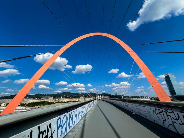 A red arch over a pedestrian bridge in Torino, Italy that connects the shopping district to a residential area. It was originally built for the 2006 Winter Olympics to connect the Olympic Village to the shops and tourist areas.