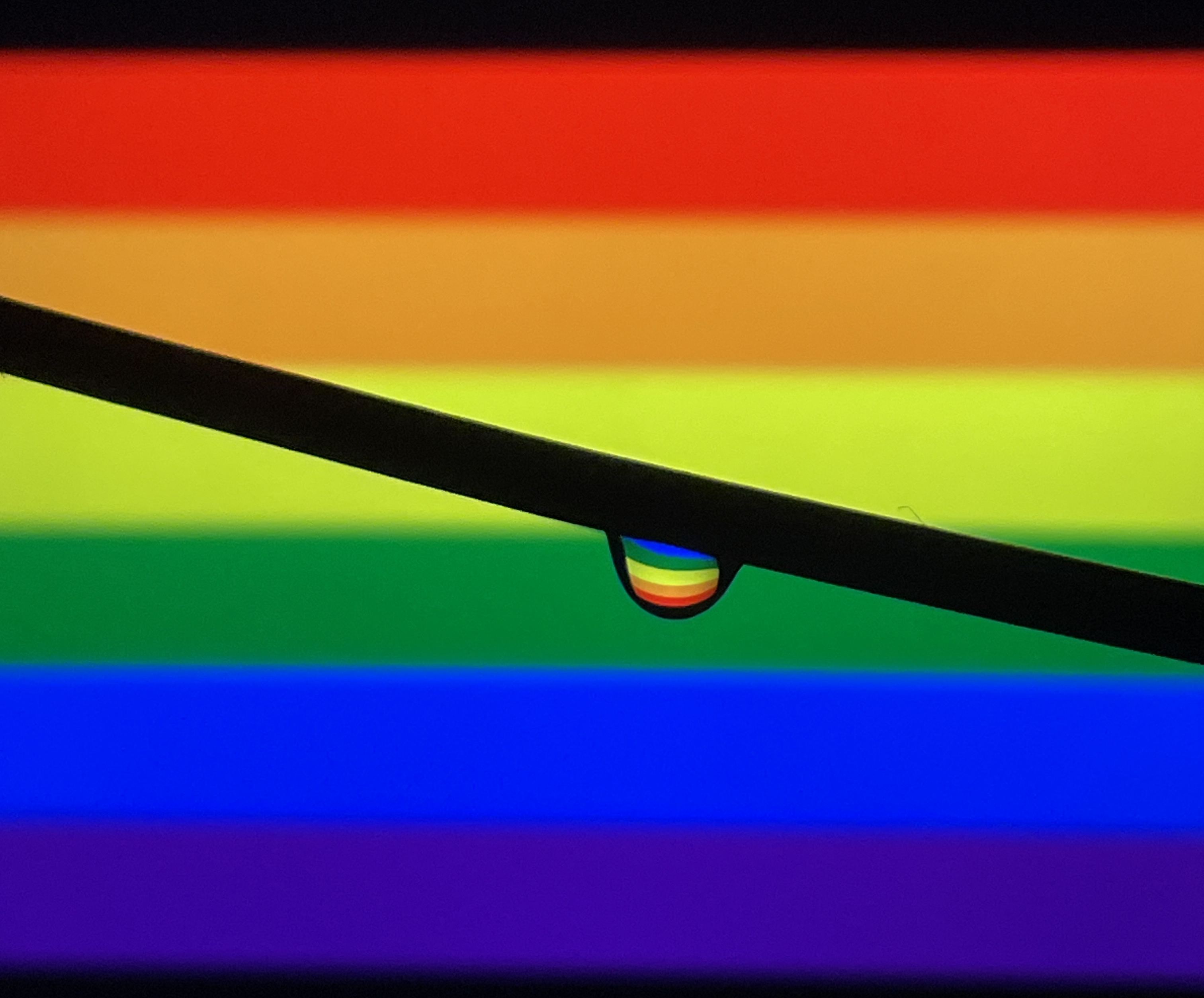 A water droplet with Pride Flag refelction and with the Pride Flag in background.