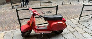 Old red scooter parked along the street.