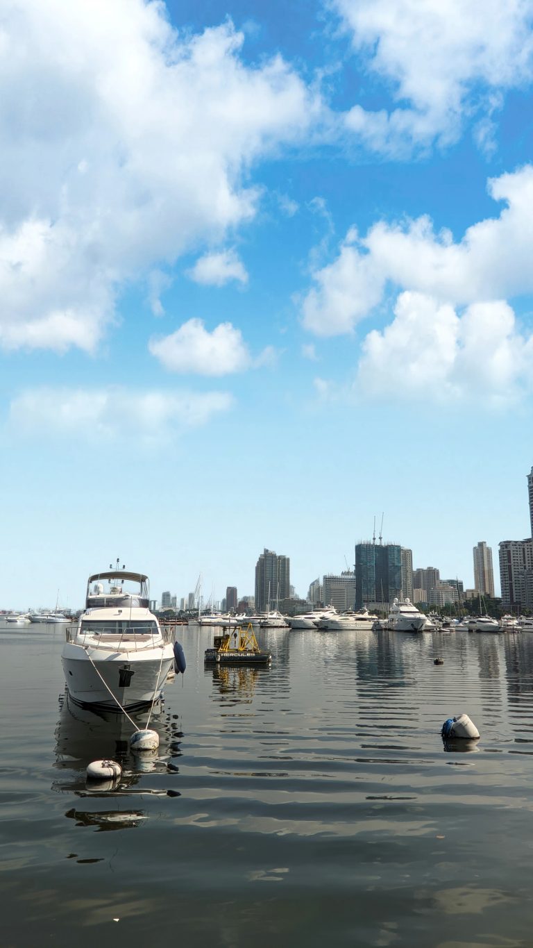 Yachts and other boats in Manila Bay with a bright blue sky and fluffy clouds overhead.