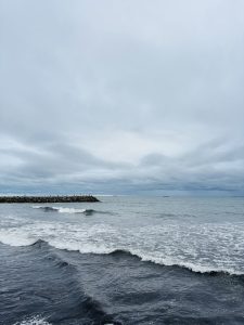  A serene ocean view with moderate waves, a partially cloudy sky, and a rocky breakwater extending into the water.
