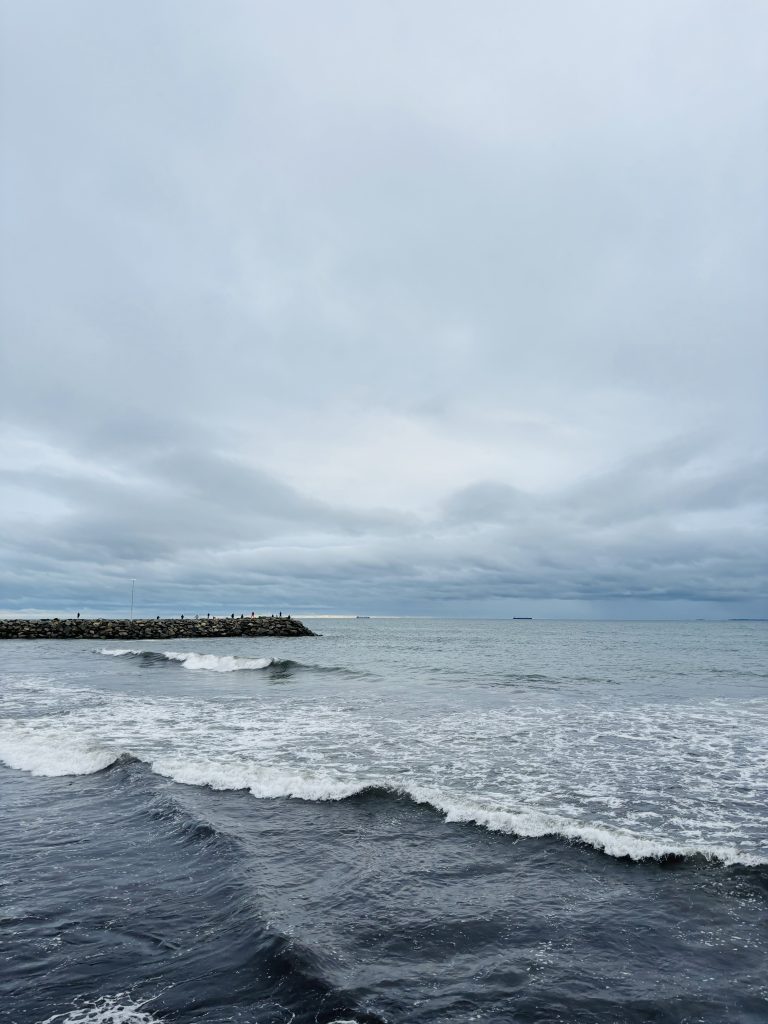 A serene ocean view with moderate waves, a partially cloudy sky, and a rocky breakwater extending into the water.