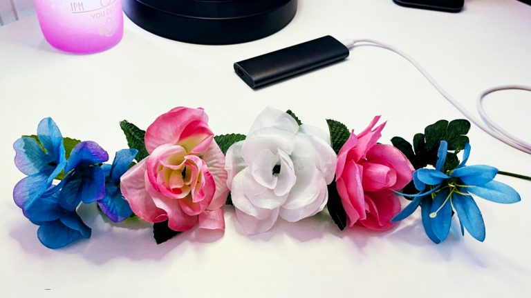 Five fake flowers arranged in the order of the trans pride flag of blue, pink, white, pink, blue