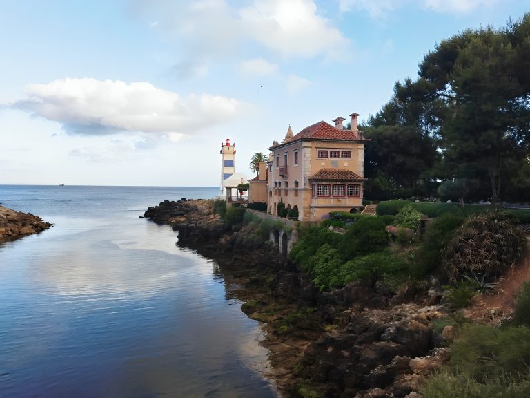 Tranquil coast with a charming house, lighthouse, and lush greenery.