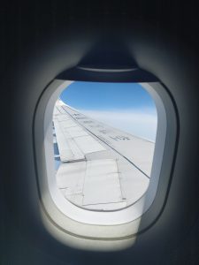 View larger photo: View from an airplane window, showing the aircraft's wing, and a blue sky with some clouds.