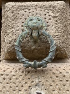 Metal ring attached to a wall with a lion's head, also made of metal.