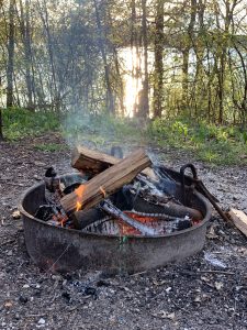 Campfire burning inside a metal ring overlooking a lake through narrow trees (YMCA Camp MacLean, Burlington, Wisconsin)