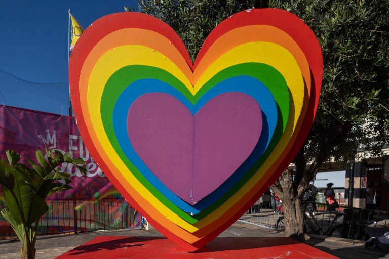 A rainbow heart with a tree and city street in the background.