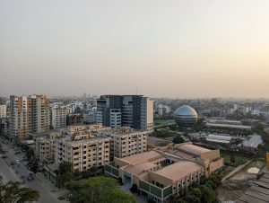 View larger photo: A cityscape with many buildings, including one shaped like a sphere. Cars and pedestrians can bee seen from a distance on the streets.