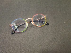 A pair of round eyeglasses with rainbow-colored rims lying on a black textured surface.