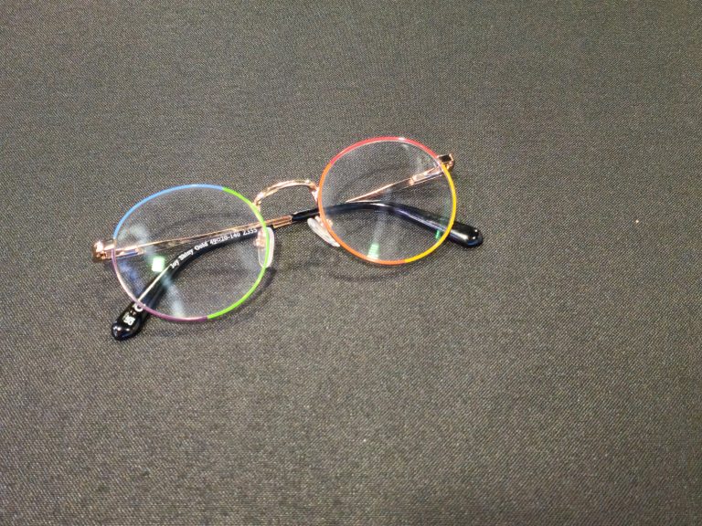 A pair of round eyeglasses with rainbow-colored rims lying on a black textured surface.