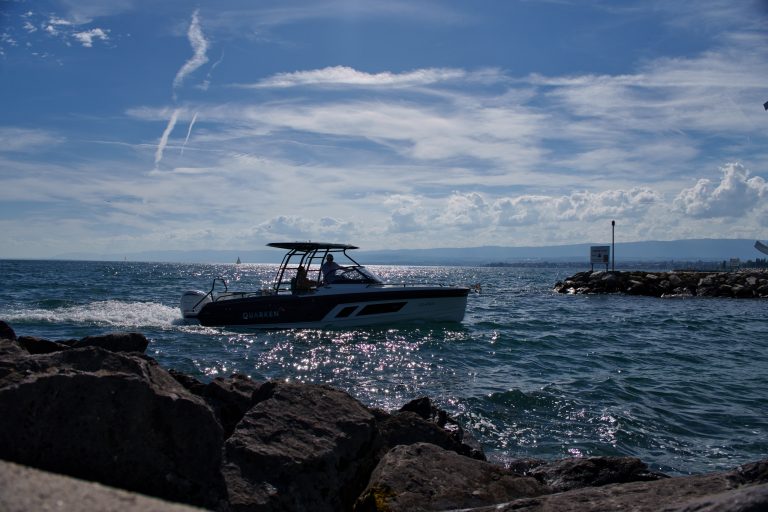 A boat on the Lausanne lake at the inlet between two rocky sides. Blue sky with fluffy clouds.