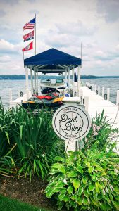 View larger photo: Single white pier with motorboat under a blue tent and a jetski in the foreground with a sign saying "Don't Blink" (Fontana-On-Geneva Lake, Wisconsin)