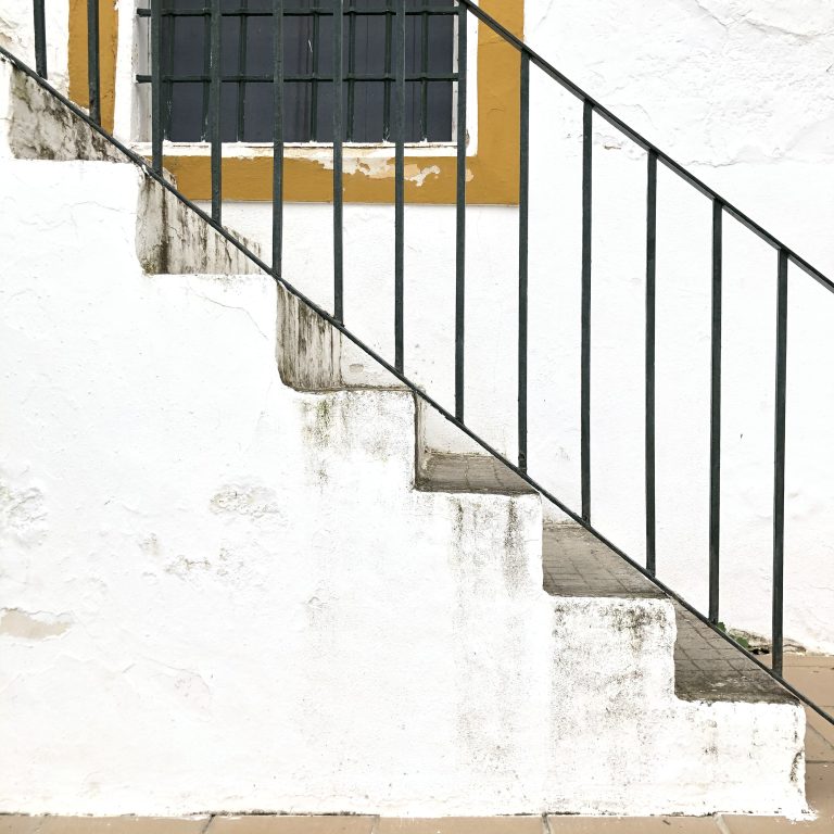 Slightly deteriorated external staircase with dark green painted railing.