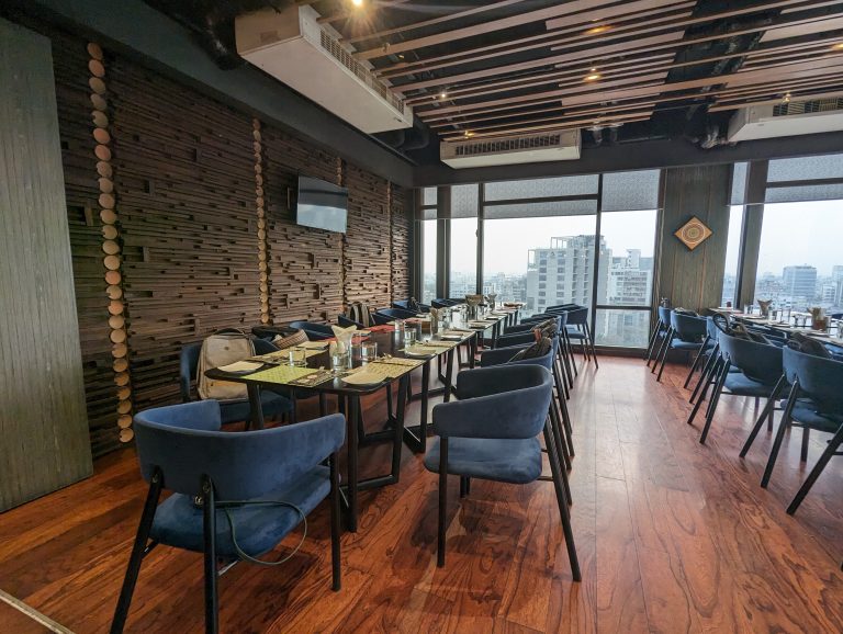 A dining table and chairs inside the Hotel. The table is ready to serve the guests and television set in the wall with is off.