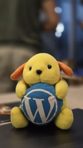 Close-up of a WordPress "Wapuu" mascotte toy sitting on a dark surface with a blurry background.