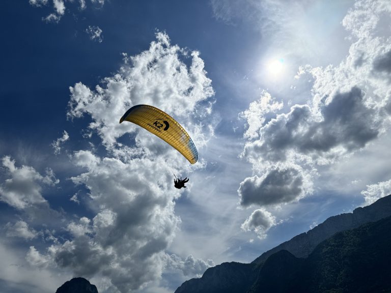 A person paragliding over lake annecy. Blue sky in the background with wispy clouds.