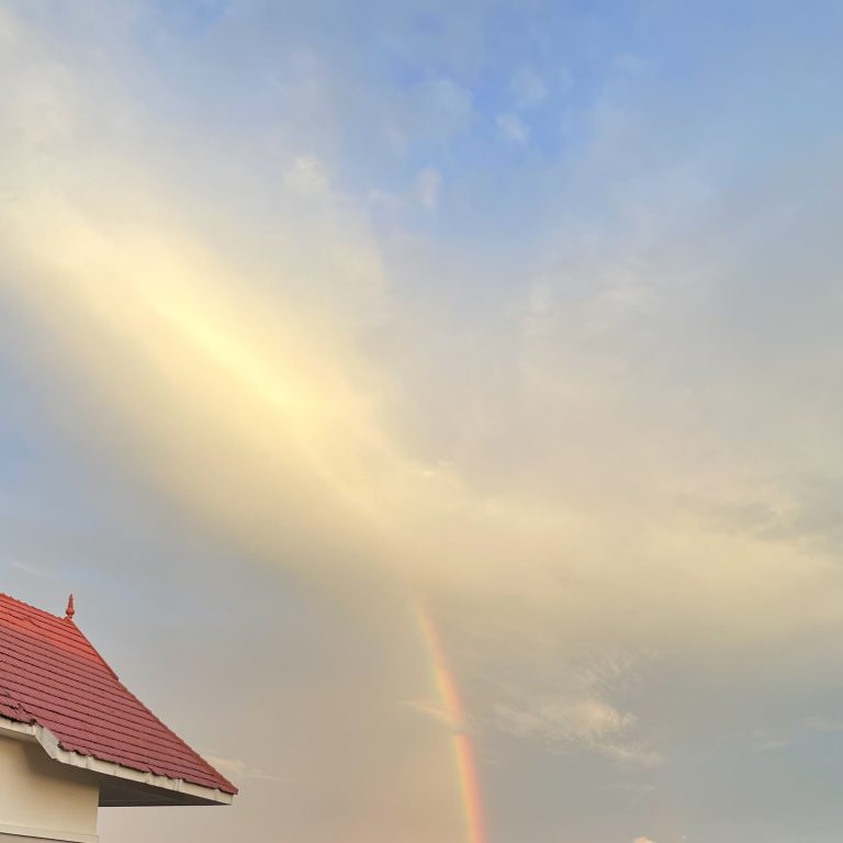 A rainbow in Kochi on the sky on a bright sunny evening with a red building roof by the side.