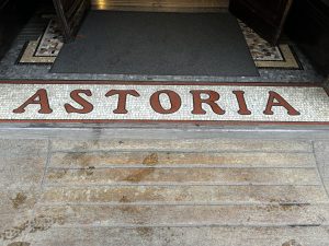 A hotel name "Astoria" embedded in the street in ornate mosaic tile.