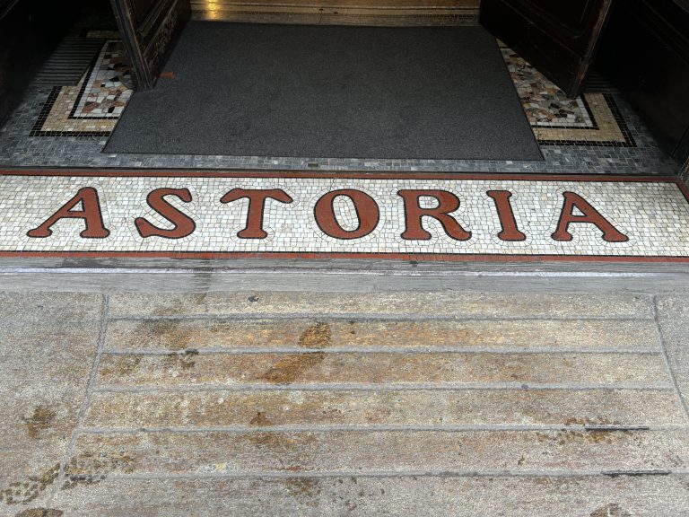 A hotel name “Astoria” embedded in the street in ornate mosaic tile.