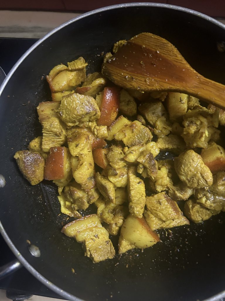 Cooked pieces of pork meat in a black frying pan with a wooden spatula.