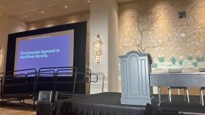 WordCamp US 2023 conference presentation set up with a projector screen on the left titled "The Enterprise Approach to WordPress Security" and an empty podium and table and chairs to the right