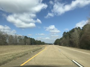 Beautiful weather on a highway surrounded by lush trees and dramatic clouds.