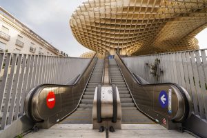 View larger photo: An outdoor escalator and stairs lead up to Metropol Parasol in Seville. The escalator on the left side has a red "do not enter" sign, and the escalator on the right side has a blue arrow indicating the correct direction of travel