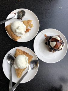 View larger photo: Three white plates hold desserts: the top left and bottom plates have pie slices with vanilla ice cream and spoons, while the right plate has chocolate cake with vanilla ice cream and chocolate syrup.