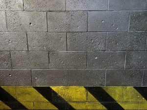 View larger photo: A black cinder block wall with a yellow caution stripe painted at the bottom. 