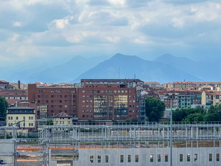 New buildings being constructed in front of older ones in Torino, Italy. Mountains in the distance appear different shades of blue.