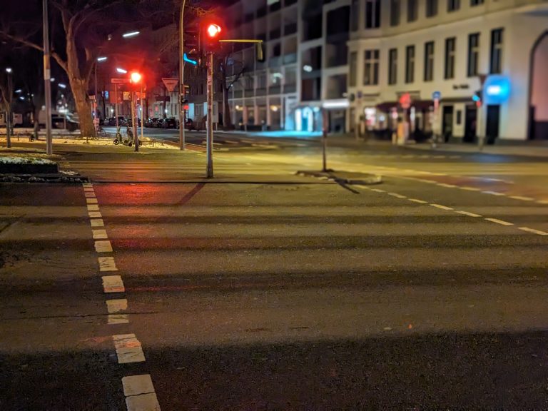 Crosswalk at night in a built-up area with red lights.