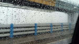 Raindrops on a car window, seen from within the vehicle. The raindrops are in focus, the background is blurred.