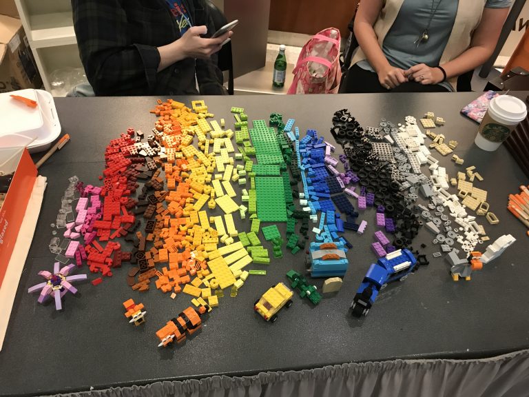 LEGO pieces laid out in a rainbow of colors on a dark grey table