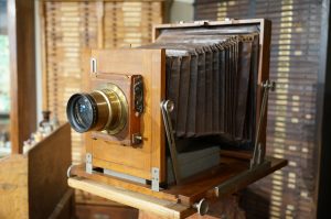 A wooden large format camera with bellows and a brass lens that belonged to Santiago Ramón y Cajal is displayed in an indoor setting. The background includes wooden drawers and various small objects.