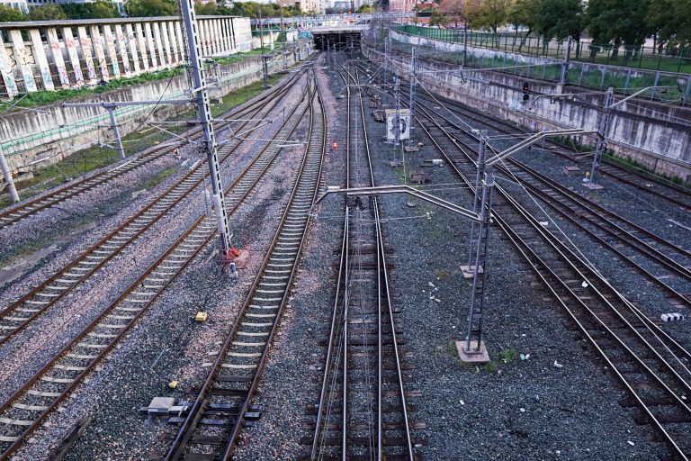 Multiple railway tracks stretch into the distance, bordered by graffiti-covered walls on the left and greenery on the right.