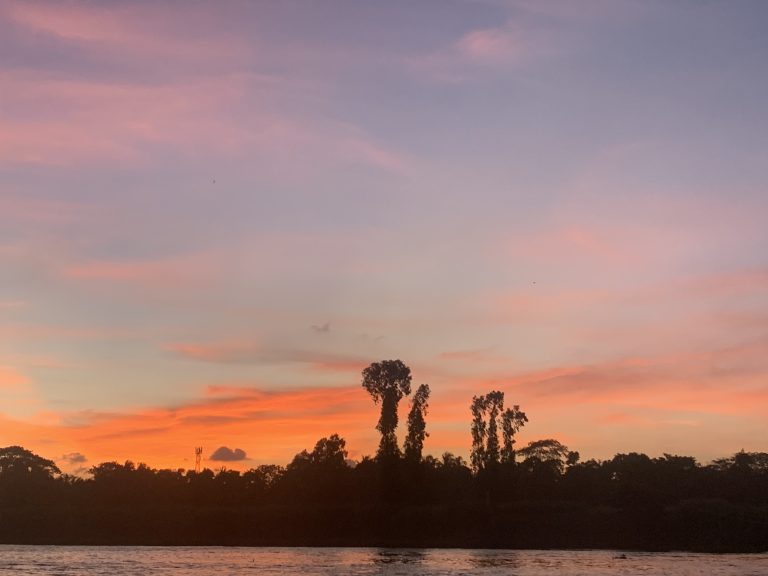 A river flows under a reddish sky at sunset, creating a beautiful and serene scene.