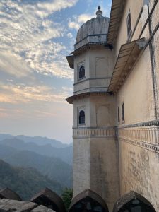 View larger photo: A historic building at Udaipur with a domed tower and arched windows, partially visible against a backdrop of distant green mountains under a partly cloudy sky.