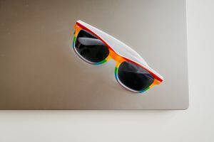 View larger photo: Pride themed rainbow sunglasses on a grey laptop with a grey background.