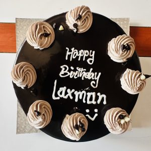 Birthday cake with chocolate topping. "Happy birthday Laxman" is written on top, followed by a smilie.