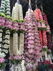 View larger photo: Hanging garlands made of various types of flowers, including white buds, pink lotus petals, red and white buds, and green leaves, displayed in a flower market.